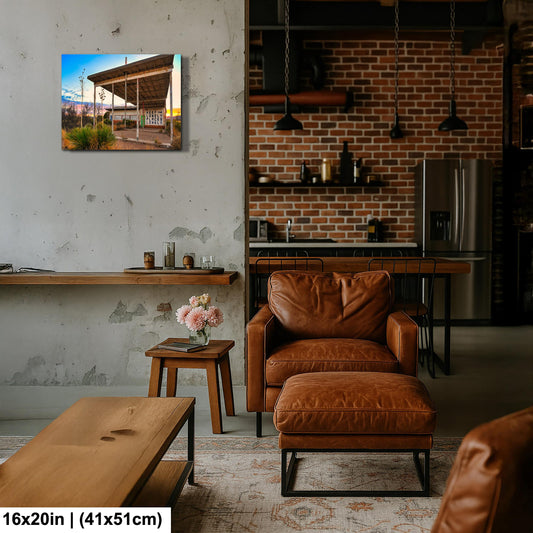 a modern living room with a brick wall, a wooden table, a leather armchair, and a wooden coffee table. There is a painting of a building on the wall, and a vase of flowers on the table.